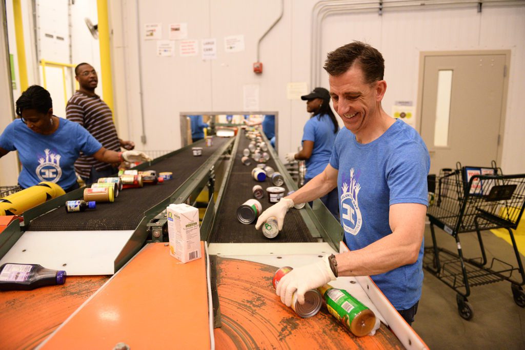 A Capital Impact employee helps sort canned goods on a conveyor belt.